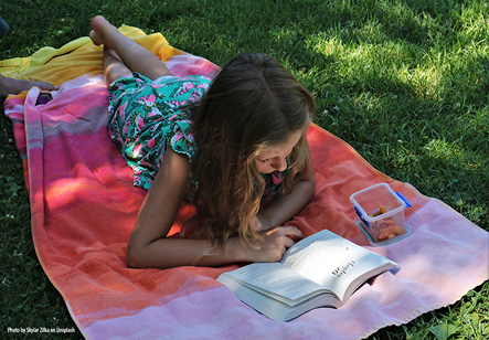 Girl lying on picnic blanket reading